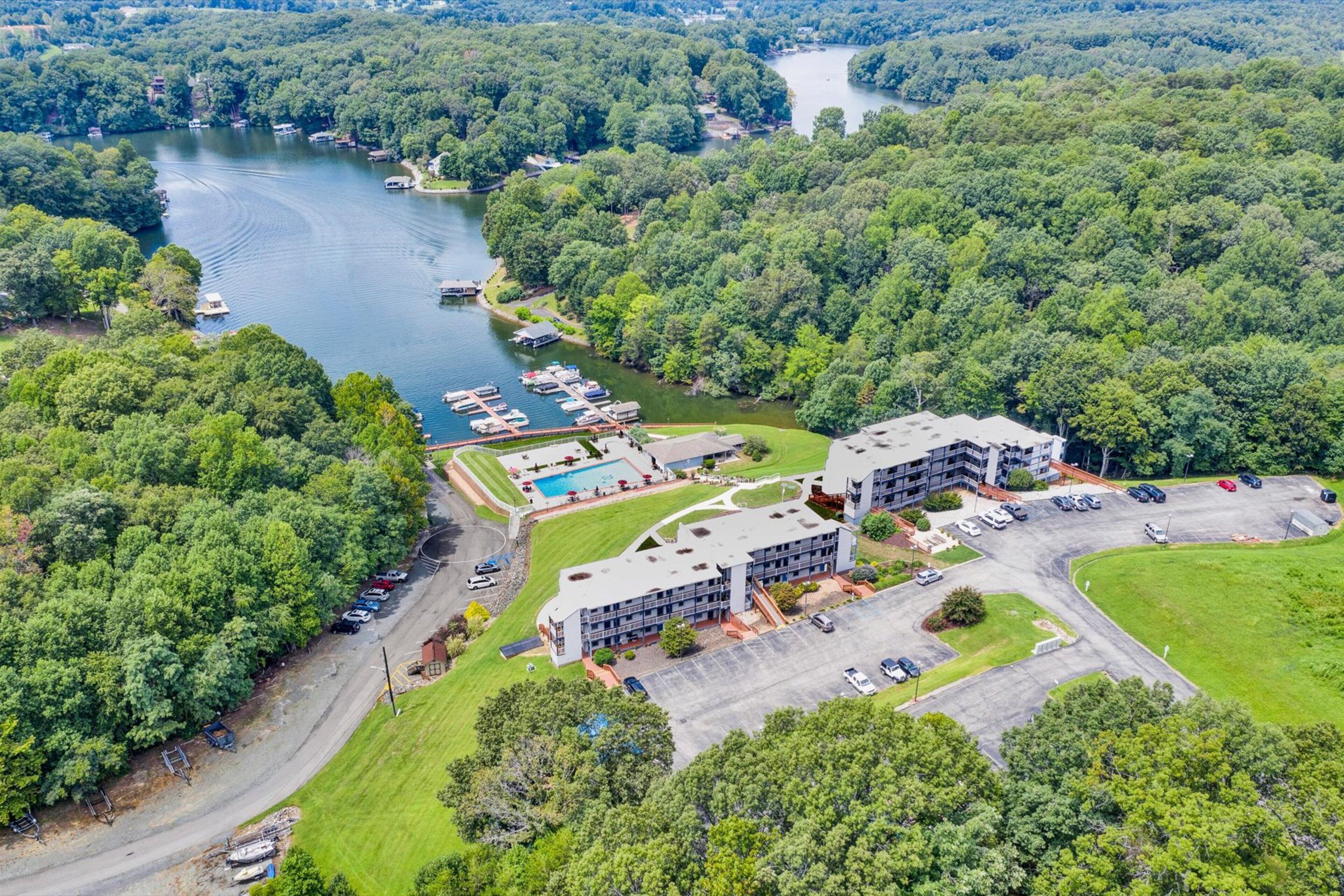 Eine Vogelperspektive zeigt ein Hotel mit mehreren Gebäuden, eine Marina mit Booten und einen See, der von dichtem Wald umgeben ist.