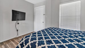 A bedroom with a bed, a television mounted on the wall, a door, and a window with blinds. - Reel Simple - Waterfront Striper's Landing Condo With Views, Pool & Boat Launch - Near Dining (Moneta)