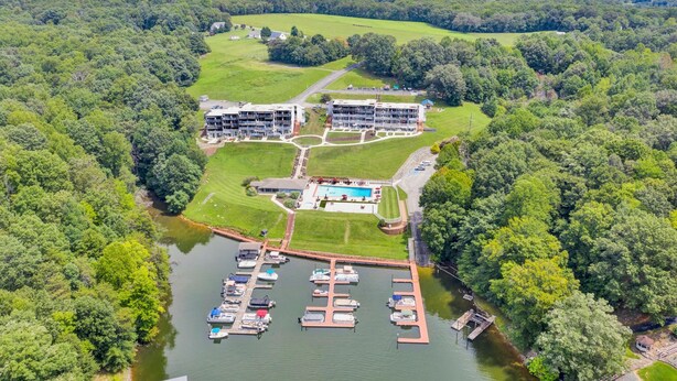 An aerial view of a resort with multiple buildings, a marina with boats, and a large swimming pool surrounded by greenery. - Reel Simple - Waterfront Striper's Landing Condo With Views, Pool & Boat Launch - Near Dining (Moneta)