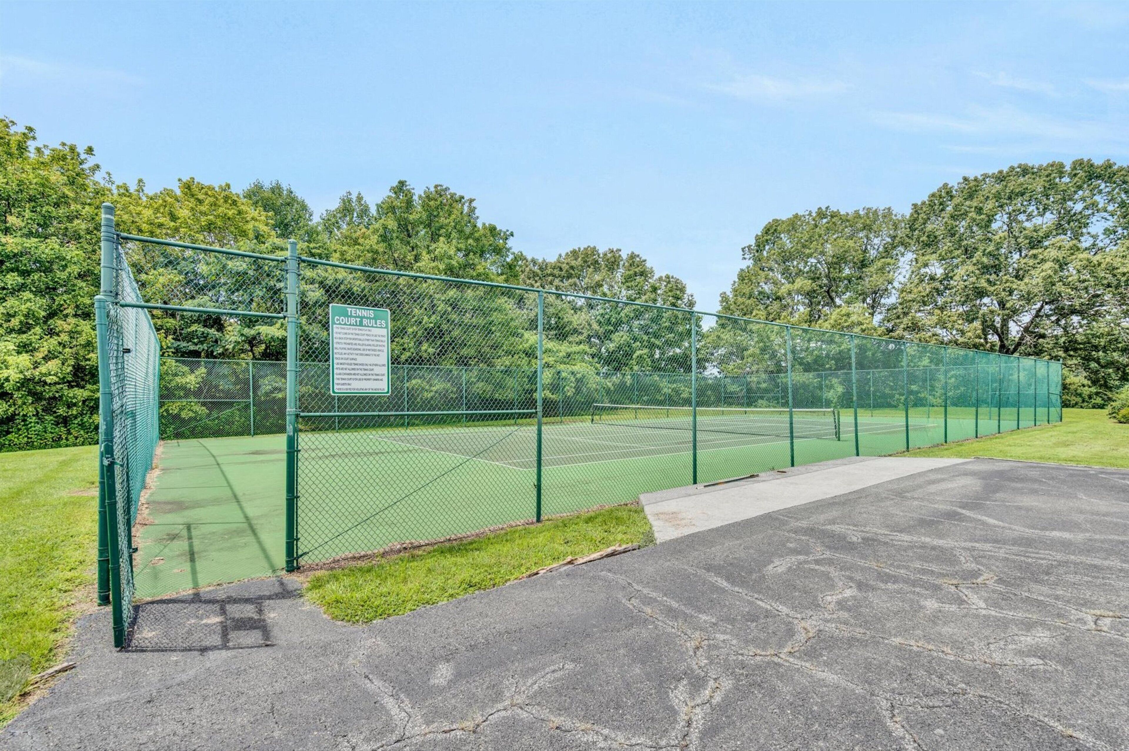 Ein Tennisplatz mit grünem Zaun, einem Schild und Bäumen im Hintergrund.