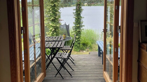 A wooden deck with a table and chairs, overlooking a lake with trees and a distant shoreline. - Charming and attractive house! (Prässebo)