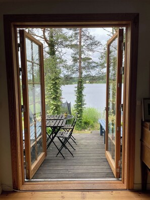 Een houten terras met een tafel en stoelen, met uitzicht op een meer met bomen en een verre oever.
