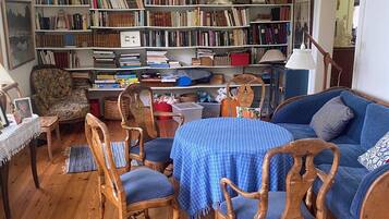 Una sala de estar acogedora con piso de madera, una mesa azul a cuadros, sillas de madera, un sofá azul y una estantería llena de libros y objetos decorativos.