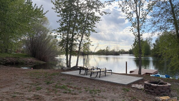 A lakeside park with benches, a fire pit, and a dock.