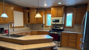 A kitchen with wooden cabinets, a stainless steel refrigerator, a microwave, a stove, and a sink.