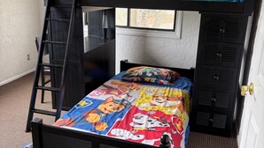 A bunk bed with a colorful bedspread, a ladder, and a window with a view of trees.