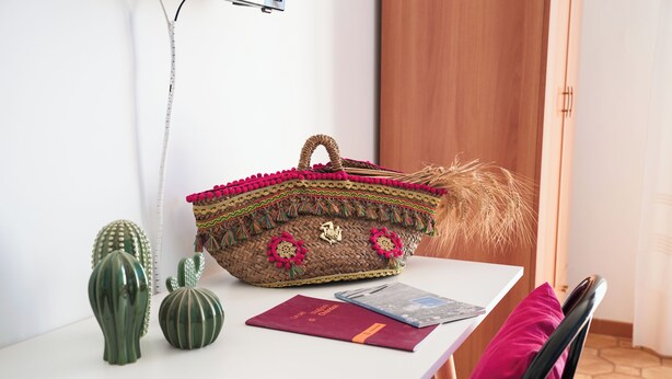 Uma mesa com uma sacola trançada, duas esculturas de cactos e um livro vermelho.