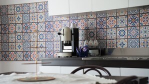 Uma cozinha com azulejos estampados, uma máquina de café e uma mesa de jantar com cadeiras.