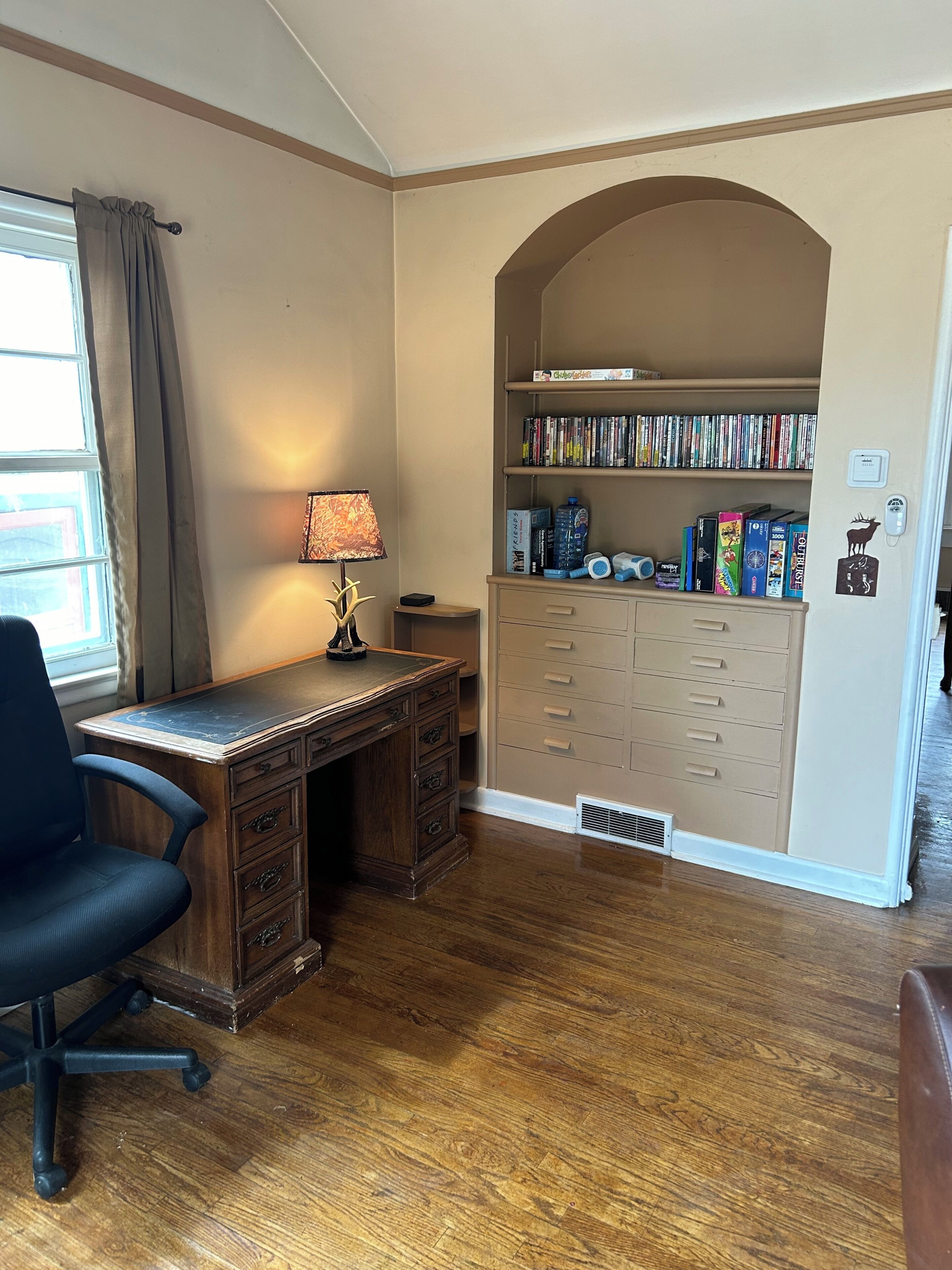 A study room with a wooden desk, chair, bookshelf, and a lamp.