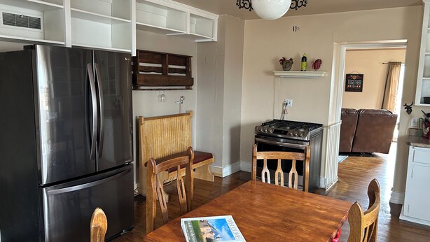 A kitchen with a black refrigerator, wooden chairs, a wooden table, a gas stove, and a hanging light fixture. - Family friendly house in the center of Walden, CO (Walden)