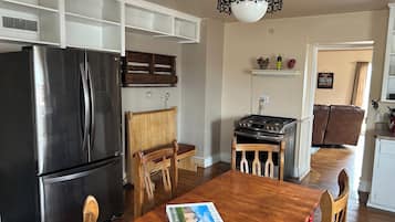 Une cuisine avec un réfrigérateur noir, des chaises en bois, une table en bois, une cuisinière à gaz et un luminaire suspendu.