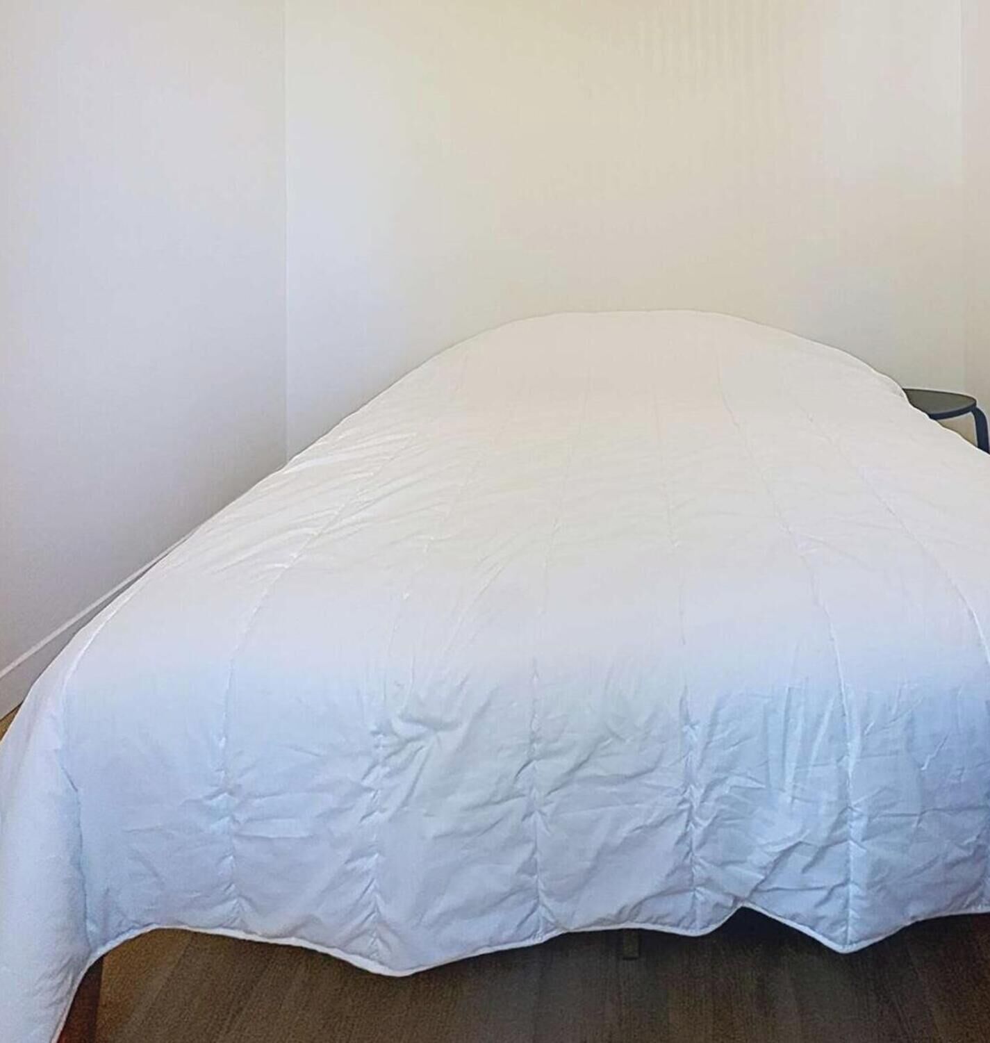 A bed with a white bedspread in a room with plain walls and a wooden floor.