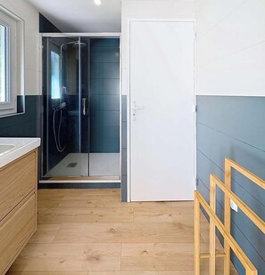 A modern bathroom with a glass shower enclosure, a wooden vanity, and a white door. - Authentic house in the heart of Lacanau Ocean (LACANAU OCEAN)