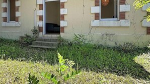Ett hus med en skylt med texten ”MELUSINE” ovanför dörren, en liten veranda och ett fönster med en hängande lampa.