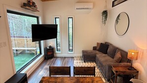 Een moderne woonkamer met houten plafond, een grote televisie, een bank, een eettafel en uitzicht op het buitenleven.