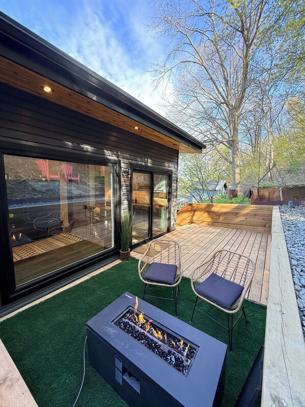 Eine moderne Außenpatio mit Feuerstelle, zwei Korbstühlen und einer Holzterrasse.
