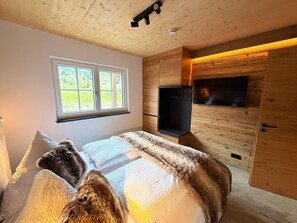 Un dormitorio con cama, almohadas, una ventana, televisión y paredes de madera.