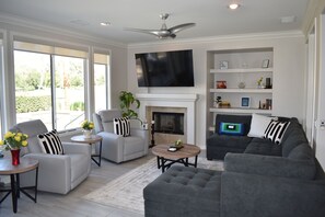 A modern living room with a fireplace, a flat-screen TV, and a large window. - Juniper Jewel- desert home with private pool and spa, views, Pickle Ball 31 days (LA  Quinta)