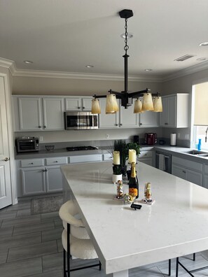A modern kitchen with white cabinets, a central island, a stainless steel oven, and a pendant light fixture. - Juniper Jewel- desert home with private pool and spa, views, Pickle Ball 31 days (LA  Quinta)