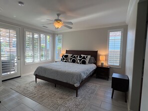 Ein Schlafzimmer mit einem Bett, einem Nachttisch, einer Lampe, einem Deckenventilator und Blick durch das Fenster.