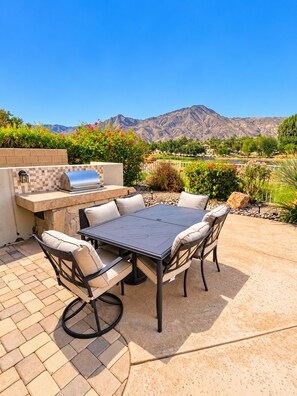 An outdoor patio with a table and chairs, a grill, and a view of mountains. - Juniper Jewel- desert home with private pool and spa, views, Pickle Ball 31 days (LA  Quinta)