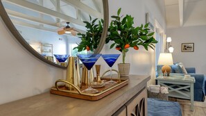 Eine Bar mit einer Holztresen, einem großen Spiegel, einem Blumentopf mit orangefarbenen Früchten und einem blauen Cocktailglas.