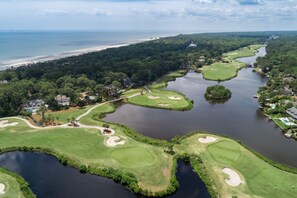 Ein Golfplatz mit mehreren Wasserhindernissen, einer Brücke und einem Strand im Hintergrund.