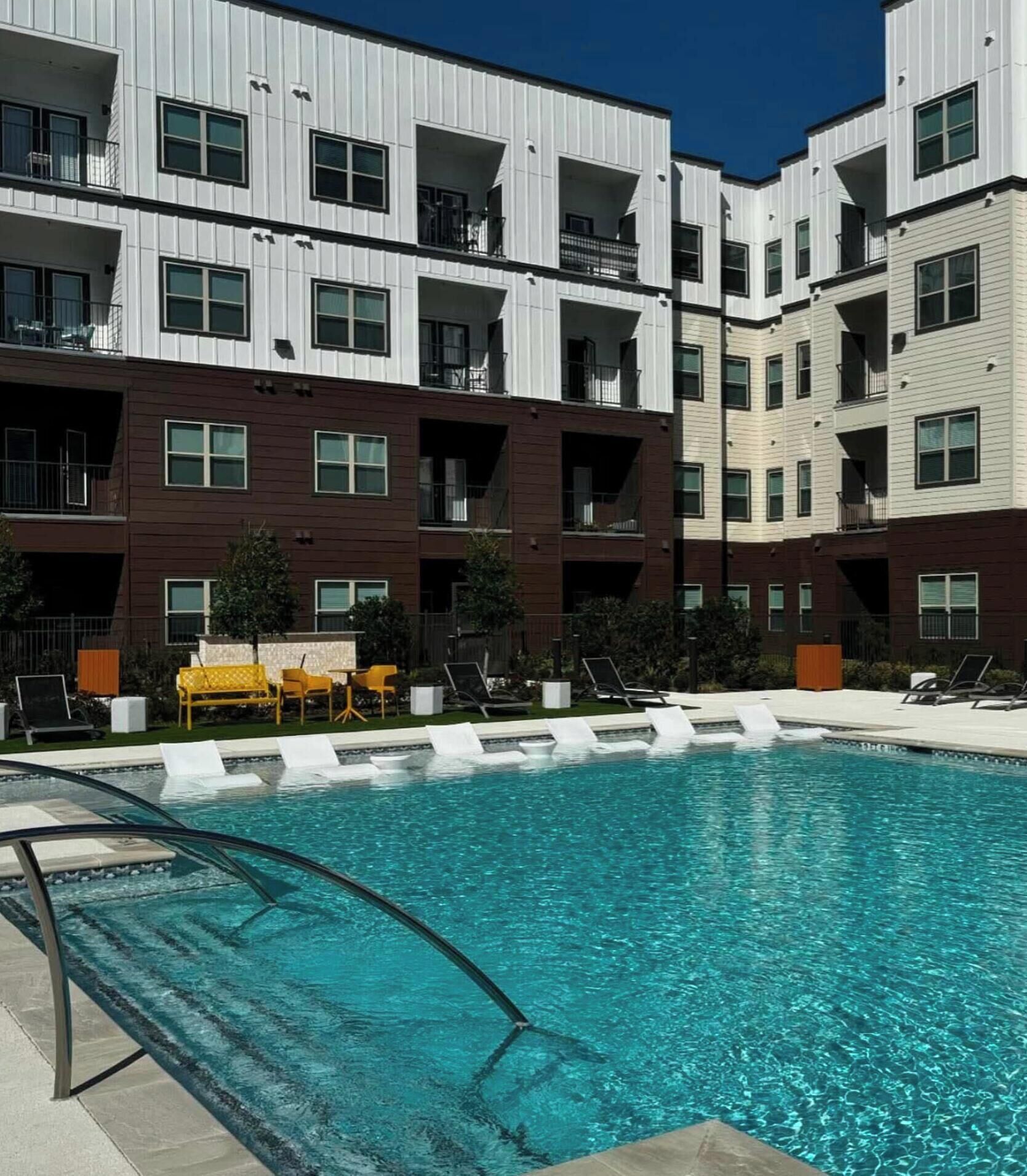 A modern multi-story residential building with a swimming pool and outdoor seating.