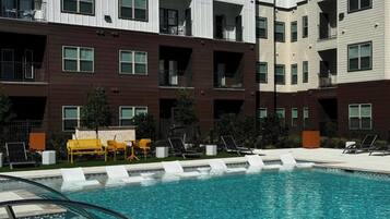 A modern multi-story residential building with a swimming pool and outdoor seating.