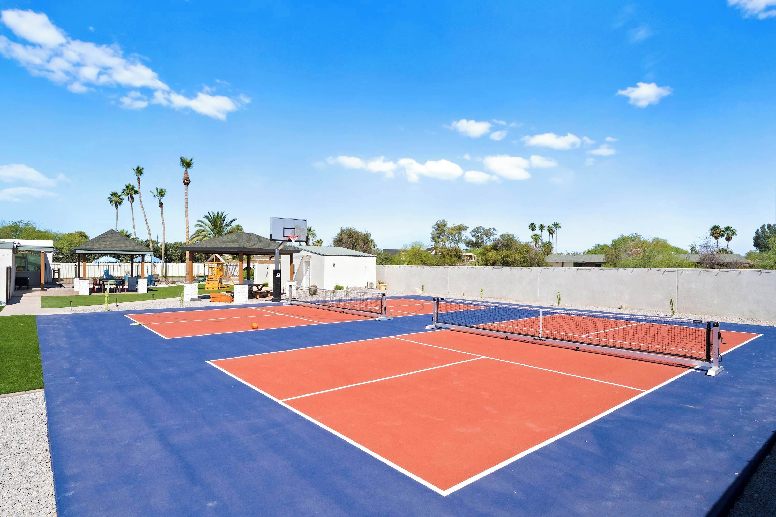 Ein Tennisplatz im Freien mit Netz, umgeben von Palmen und Gebäuden.