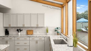 Een moderne keuken met witte kasten, granieten aanrecht, een dakraam en uitzicht op de omgeving.