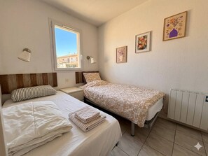 Ein Schlafzimmer mit zwei Betten, einem Fenster, Wandbildern und einer Heizung.