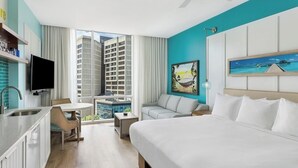 A hotel room with a bed, a desk with a chair, a sofa, a TV, and a large window with a view of buildings. - Downtown Atlanta Wyndham Studio Suite - World Cup Stay Near Stadium (Atlanta)