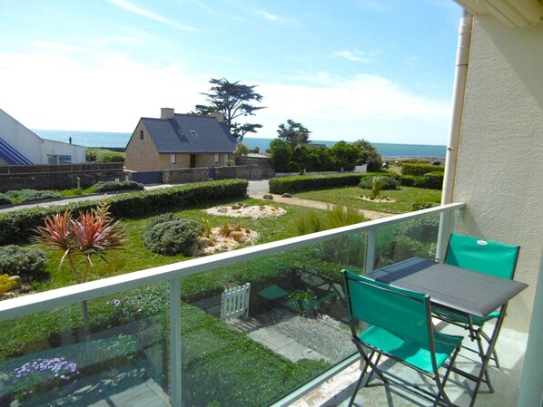 Ein Balkon mit Tisch und Stühlen, der auf einen gepflegten Garten mit verschiedenen Pflanzen und Meerblick blickt.