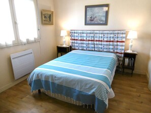 Ein Schlafzimmer mit einem Bett, zwei Nachttischen, einem Fenster, einer Heizung und einem gerahmten Bild an der Wand.