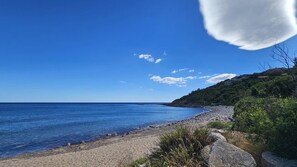 Une plage bordée d’une eau d’un bleu limpide, un rivage rocheux et une colline couverte de végétation.