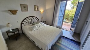 Une chambre à coucher comprenant un lit, deux tables de chevet, une commode, une lampe fixée au mur et une porte donnant sur un espace extérieur.