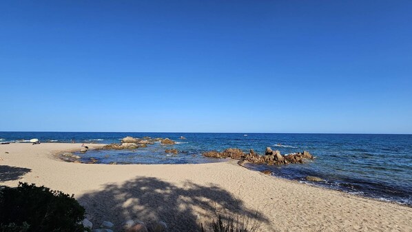 Une plage avec un ciel dégagé, une eau calme et des formations rocheuses.