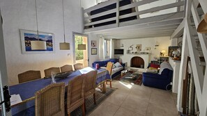 Ein geräumiger Wohnbereich mit Esstisch, Korbstühlen, einem blauen Sofa und einem Kamin.