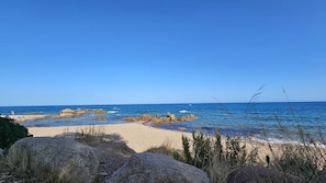 A beach with clear blue water, rocky outcrops, and a sandy path leading to the sea. - Villa TESTA—60 meters from La Testa Beach—Wi-Fi (ZONZA)