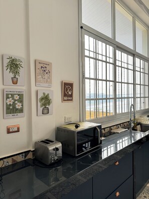 Une cuisine dotée d’une grande fenêtre, d’un grille-pain, d’un four à micro-ondes et de divers tableaux encadrés représentant des motifs botaniques accrochés au mur.