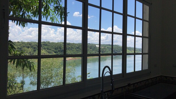A window with a grid pattern, a sink, and a view of a river and forest. - The house on the Iguazú River (Puerto Iguazú)