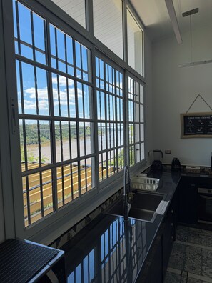 Una cocina con un ventanal amplio, un lavamanos, un hervidor y una pizarra con escritura.