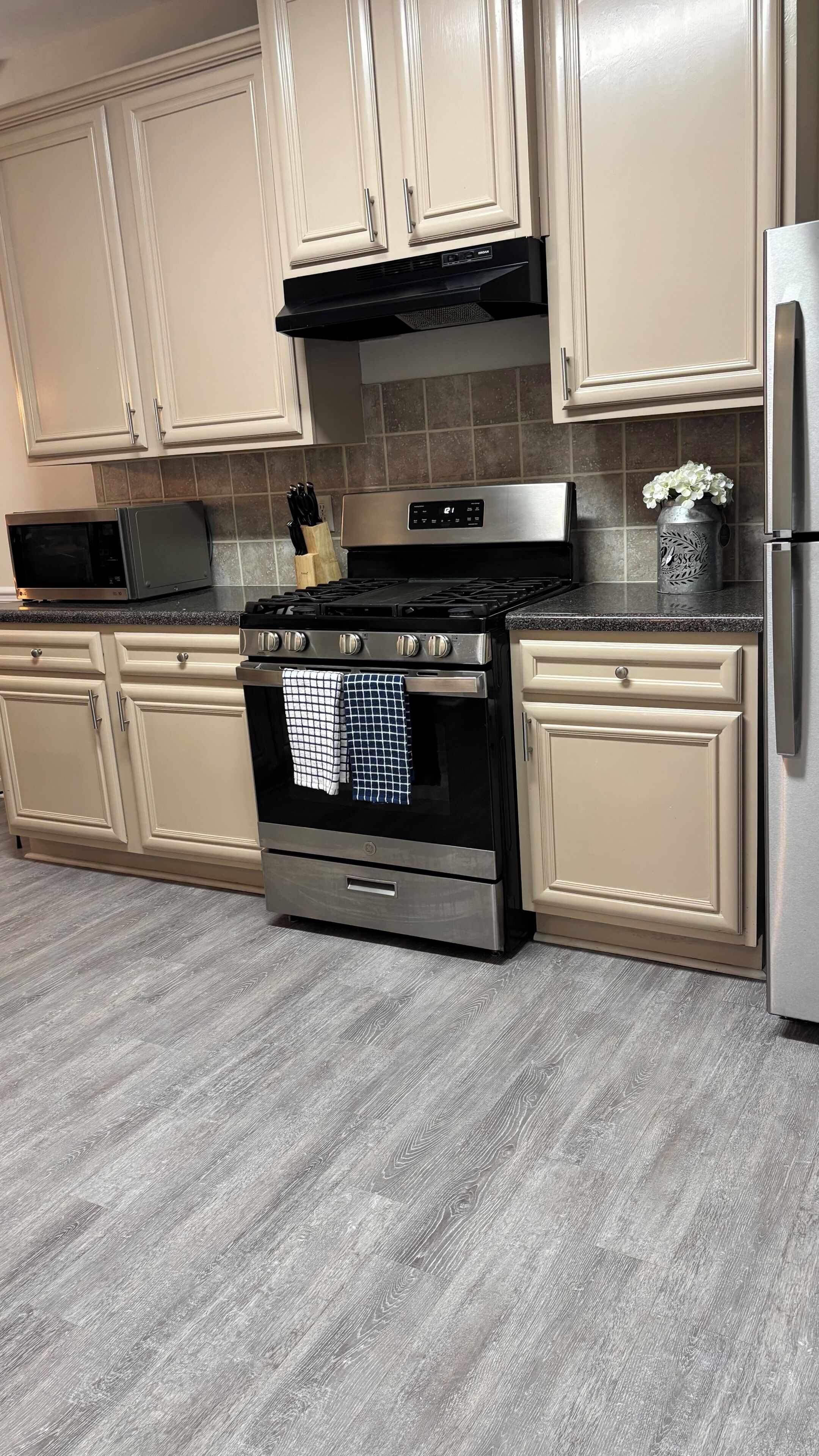 Una cocina con armarios blancos, estufa de acero inoxidable, microondas y refrigerador.