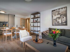 Un soggiorno moderno con un divano, un tavolino da caffè, un'area pranzo con sedie e un tavolo, una libreria e un quadro appeso al muro.