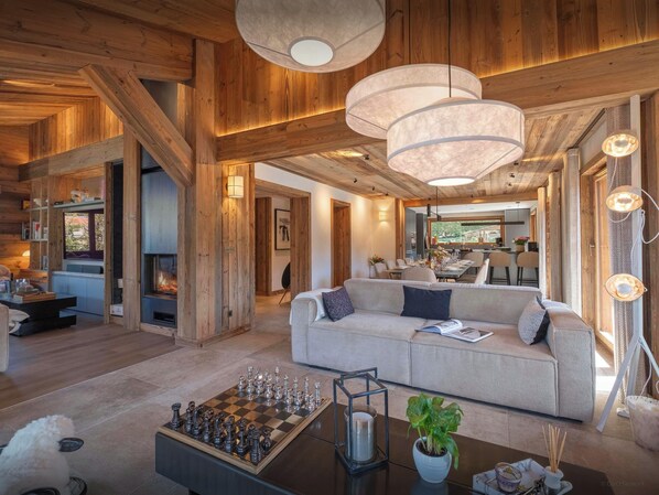 A spacious living area with a fireplace, wooden beams, a sofa, and a chessboard.