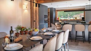 Un comedor moderno con techo de madera, una cocina al fondo y vista a espacios verdes.