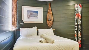 Une chambre d’hôtel avec un lit, des oreillers, un tableau encadré au mur, un objet décoratif fixé au mur et des skis appuyés contre le mur.