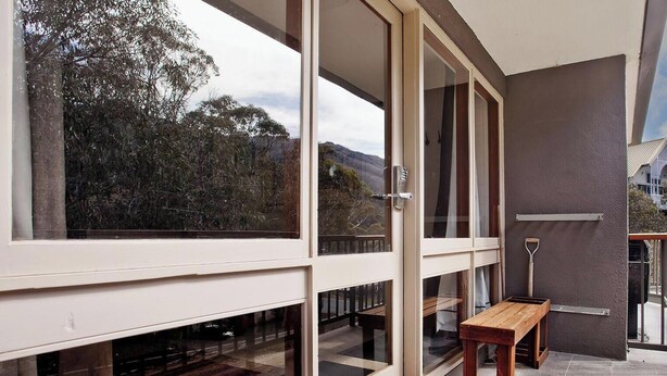 Un balcon avec un banc en bois, de grandes fenêtres et une vue sur les arbres et les collines.