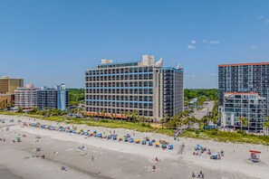 A beachfront hotel with multiple floors, a sandy beach in front, and several umbrellas. - Stunning 3bedroom ocean front at Ocean Reef (Myrtle Beach)